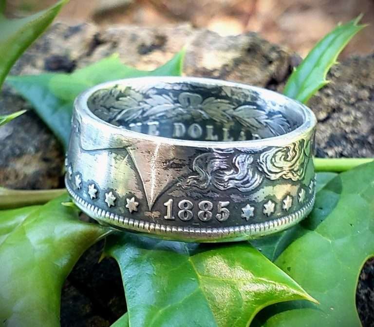 A Morgan silver dollar ring dated 1885 resting on green leaves